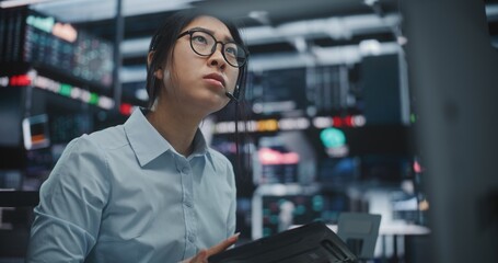 Fototapeta premium Asian Woman Frantically Cross References Real Time Financial Data on Multi Monitor Workstation and Tablet. Female Reports Critical Market Information Contact on Smartphone. Urgent Communication.
