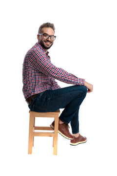 Side view of happy casual man sitting on stool