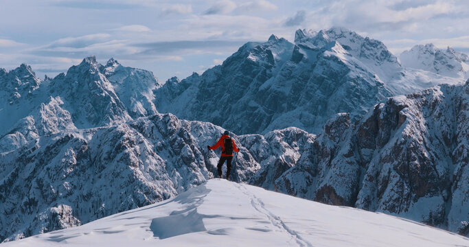 Ski mountaineer standing on a snowy cliff in the Dolomites with majestic alpine peaks in the background, capturing winter adventure, solitude and breathtaking mountain scenery.