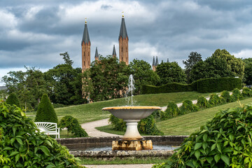 Obraz premium View from the Palace Park in Neustrelitz towards the Palace Church, Mecklenburg-Western Pomerania, Germany, with a cascading fountain and bench in the foreground.