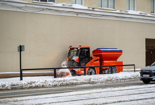 A compact universal machine for cleaning city streets clears the sidewalk of snow. Winter city background.