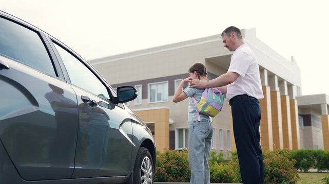 caring father by car sees child kid girl daughter school, happy family, school building background, father helps child kid girl daughter put backpack, girl with school backpack goes school, man father