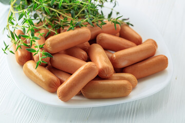 Naklejka premium Boiled sausages with thyme on a white wooden table.