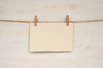 A sheet of handmade paper hanging from a twine against a wooden background