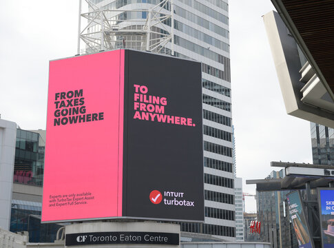 wide view of digital billboard advertising for Intuit with catchy slogans above entrance to CF Toronto Eaton Centre, facing Sankofa Square