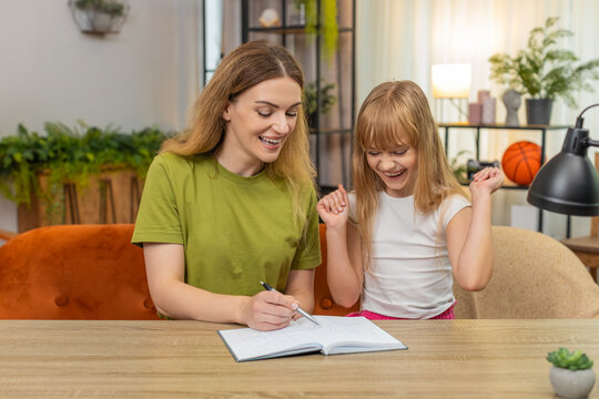 Mother and daughter at home draw grid play tic tac toe rounds tally score in notebook and pen. Woman and girl at table trade moves cross and noughts laugh rematch friendly game keep record time well