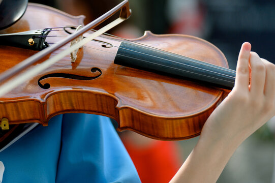 Close-up of violin being played by musician in blue shirt outdoors