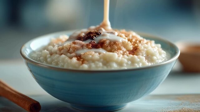 Pouring milk into a bowl of rice pudding with cinnamon. Hot breakfast porridge with steam rising