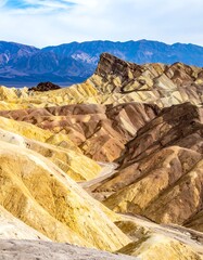 Eroded badlands with gold, tan, & brown strata rise to meet distant blue mountains