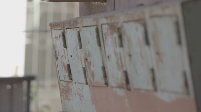 A close up view of a row of old, rusty metal mailboxes with peeling pale paint, mounted on a wall in a weathered and dilapidated outdoor urban setting.

