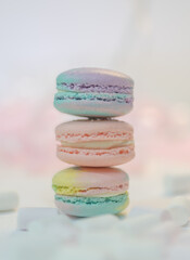Fototapeta premium Stack of colorful macarons in pastel shades on light background. French almond cookies with creamy filling. Minimal dessert composition with soft tones and copy space.
