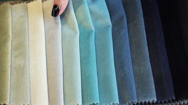 woman touches, irons and chooses blue fabric from fabric samples for curtains, textiles and furniture. professional selection of fabric in the salon, interior design, cozy home, tactile sensation