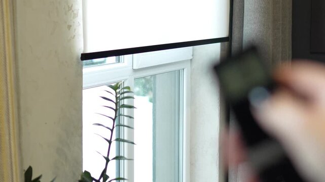 woman controls the remote control for the automatic system of opening and closing the roller blind. professional window shading salon, electric drive, elite technology, curtains on the remote control