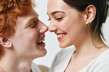 Fototapeta premium Couple smiling closely with joyful expressions in casual clothing on bright background. Young man and woman showing affection and happiness in intimate moment with natural light.