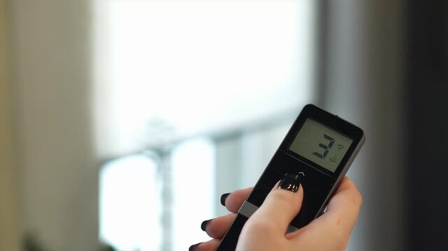 woman controls the remote control for the automatic system of opening and closing the roller blind. professional window shading salon, electric drive, elite technology, curtains on the remote control