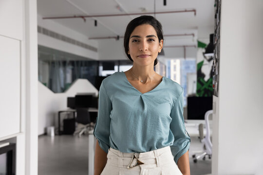 Portrait smiling young adult Brazilian woman corporate worker startup founder manager executive successful business professional looking at camera posing for personal branding picture in modern office