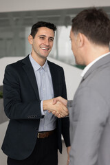 Smiling young adult Latin businessman exchanging handshake with male business partner in office satisfied with making successful mutual agreement based on partnership trust cooperation. Vertical image