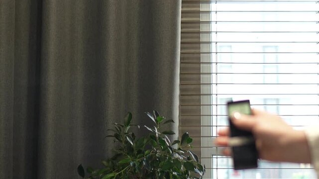 woman controls the remote control for the automatic system of opening and closing curtains. professional window shading salon, electric drive, servo drive, elite technologies, curtains on the remote