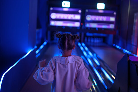 The girl is happy to play bowling and score a strike. The dark neon game room of the entertainment center