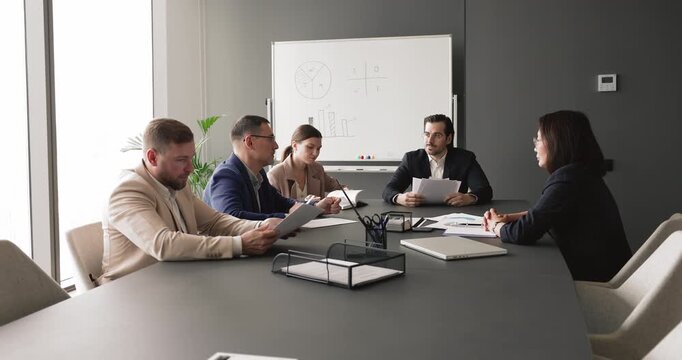 Diverse businesspeople sitting at conference table reviewing printed reports and discussing strategy during team meeting, engage in teamwork, decision-making, project evaluation, corporate planning