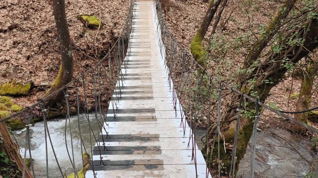 A serene view of the musical bridge spanning the Asopos River, a charming wooden rope bridge crafted to resemble piano keys, set within the lush landscape of Pavliani Recreational Park in Greece.