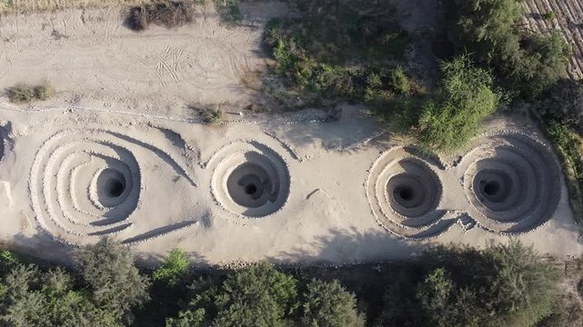Cinematic drone shot of the ingenious filtering galleries and spiral vents used for irrigation in the Nasca desert.