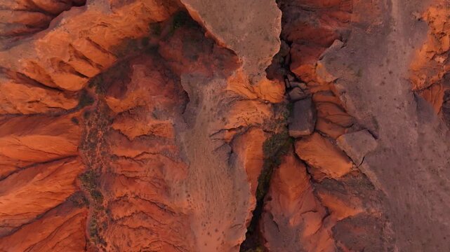 Cinematic top-down drone flight forward revealing the surreal eroded red rock maze of Kok-Moinok 2 - deep crevices, layered clay-sand structures, and sparse vegetation below.