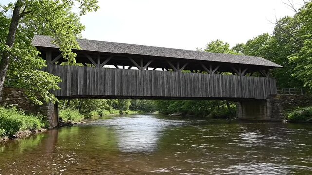 Old wooden covered bridge spans scenic river in lush forest