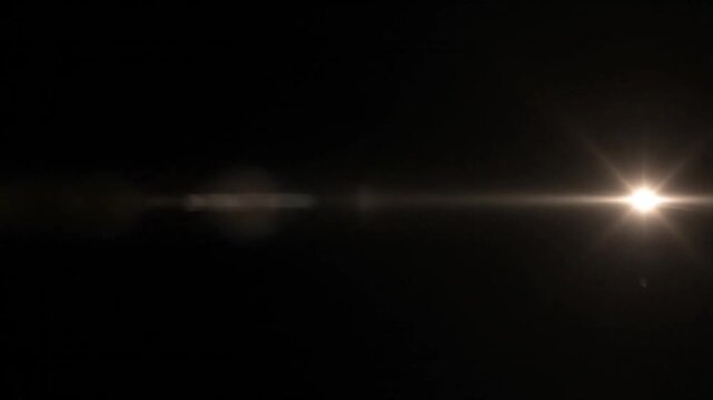 A bright, warm-toned lens flare effect sweeps horizontally across a dark, black background, creating a dynamic and ethereal light streak.