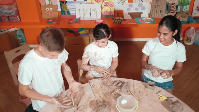 Top view of smart diverse student sculpt clay at pottery class or workshop. Smart high school children with mixed races playing with modeling clay or creating artwork in creative activity. Edification
