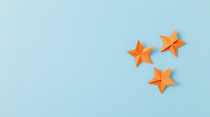 Obraz premium Soft blue background with three small orange paper star decorations placed on the side, minimal and clean composition, pastel tone, soft lighting, simple and elegant design.