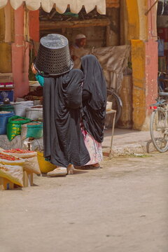 Local women in black burqas -one carrying a large bucket on her head- shopping at a stall on a side street of the central souk. Rissani-Morocco-168