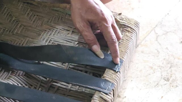 Close up of craftsman hands repairing woven furniture seat by attaching rubber straps with yellow staple gun and hammer