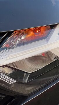 Front car headlight with blinking amber turn signal, close up modern automotive lighting detail, vehicle safety indication, daytime visibility, technology design, transportation feature system