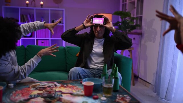 Diverse friends playing a charades guessing game with a smartphone at a home party in a living room with neon lights