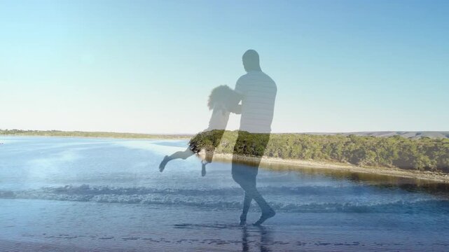Dad leaning back swinging daughter on shore for family play, with faint treeline over figures