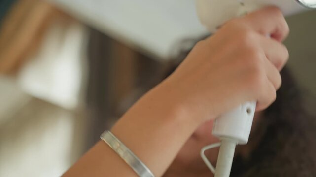Hotel bathroom guest drying curly hair in mirror closeup, towel wrapped, handheld white dryer, soft sunlight, fingers massaging roots, relaxed selfcare vibe in boutique hotel vanity with silver