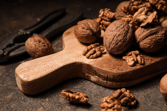 Wooden board with walnuts and nut cracker on grey grunge background, closeup