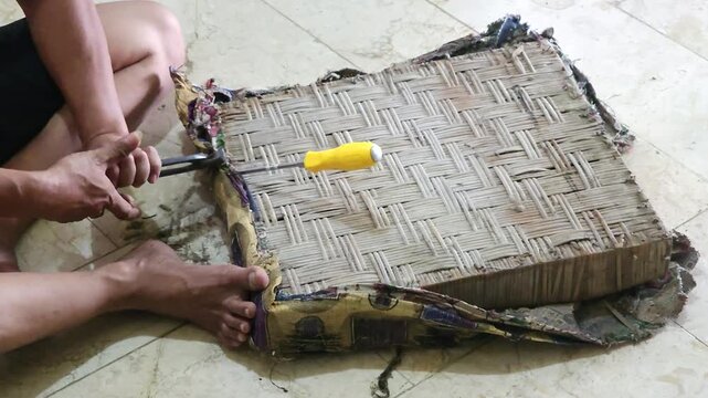 Close up of craftsman hands using carpenter pincers to remove nails from woven bamboo chair seat during furniture restoration process indoors