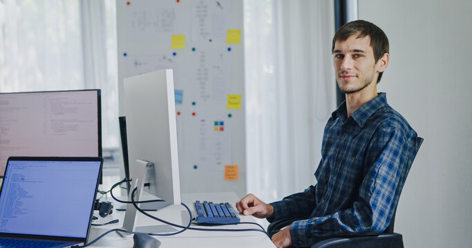 Portrait confident smiling male programmer working with robotics code AI software and looking at camera in tech office. Artificial intelligence dashboard, robotics, user interface, machine learning.