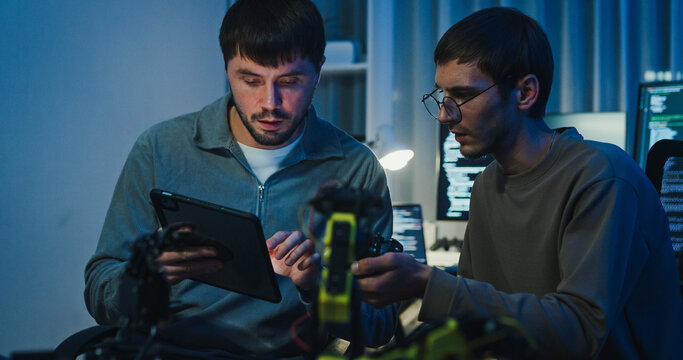 Team adult male engineer collaborate on robotic hand project using AI code solutions machine learning at tech workspace night. Artificial intelligence interface, collaboration prototype development.