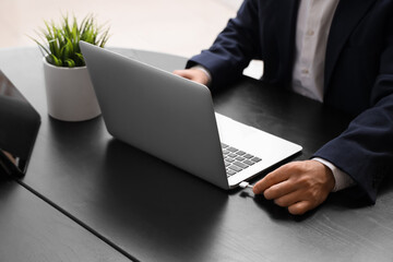 Businessman connecting charging cable to laptop in office, closeup