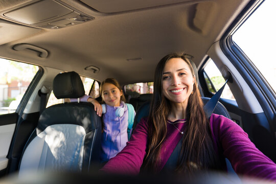 Mother driving car with daughter in backseat, both smiling, traveling to school drop off or carpool