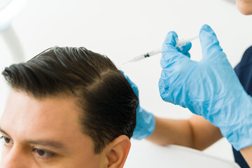 Closeup of man receiving injections for hair restoration on scalp in medical clinic with...
