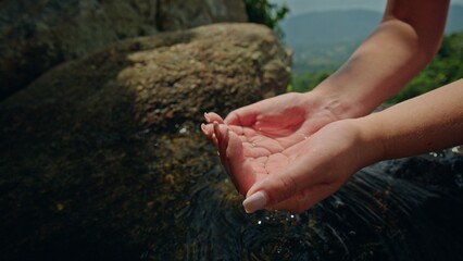 Close up of human hands gently cupping clear mountain spring water over natural stone in green...
