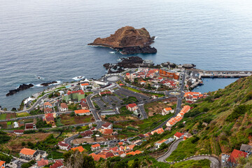 Fototapeta premium Porto Moniz coastal village on Madeira Island, Portugal. Red-roofed buildings near Atlantic Ocean. Rocky shoreline with volcanic cliffs. Scenic view of natural seascape.