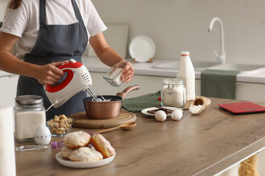 Woman whipping egg albumen with mixer at table in kitchen