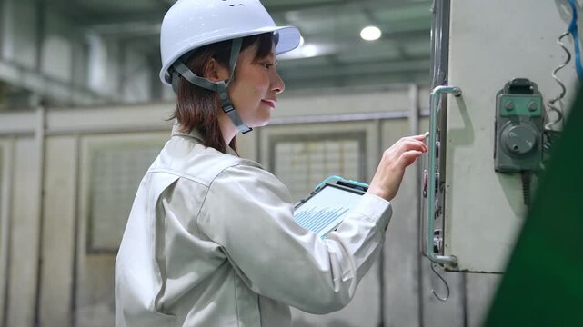 タブレットを持って工場機械を点検する女性作業員