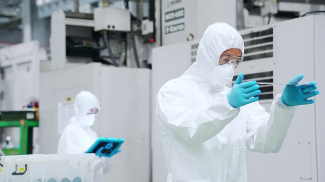 A male worker in protective clothing inspects silicon wafers at a semiconductor factory