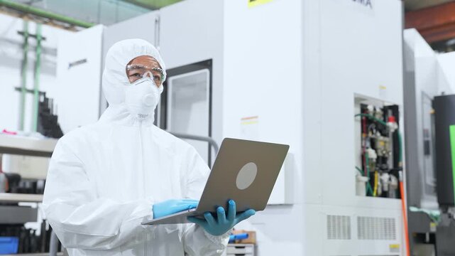 A male worker wearing protective clothing working in a factory with a laptop